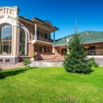 Modern luxury villa with large windows, surrounded by lush green lawn and trees.